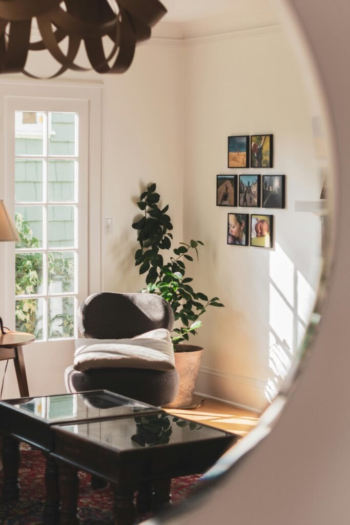 Interior of cozy light living room in retro style with comfortable chair and small table located in front of window reflected in round mirror hanging on wall